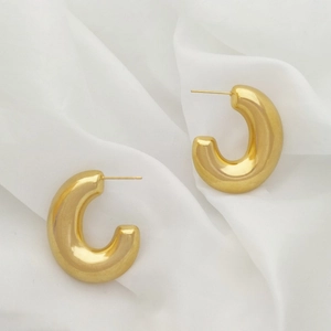 Detail shot of chunky gold U-shaped C-hoop earrings on a soft white silk background