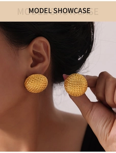 Close-up of elegant gold-plated round earrings with textured geometric pattern on model