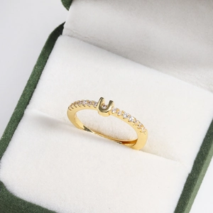 Macro view of adjustable gold-plated letter U ring with crystals in green velvet box