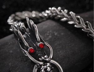 Macro shot of a silver dragon head bracelet with red rhinestone eyes and woven chain