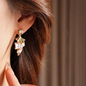 Close-up of model wearing gold leaf-shaped enamel earrings with sparkling zircon