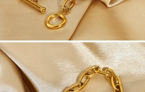 Macro shot of gold paperclip chain bracelet with OT toggle clasp on champagne silk fabric