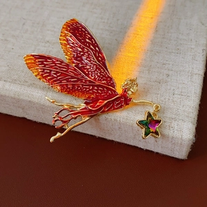 Macro view of vintage enamel fairy brooch with red wings and gold accents on fabric