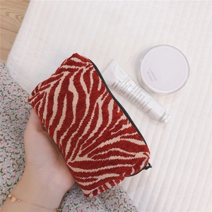 Close-up of red zebra pattern corduroy makeup bag with zipper held in hand