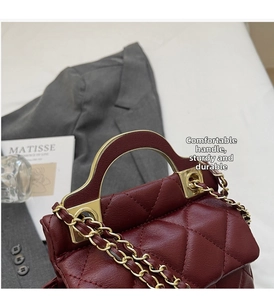 Detail of burgundy quilted handbag featuring semi-circular gold metal handle and chain strap