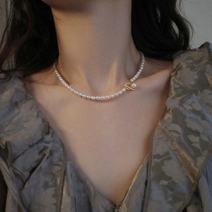 Detail of baroque pearl necklace with golden T-bar clasp worn by a model