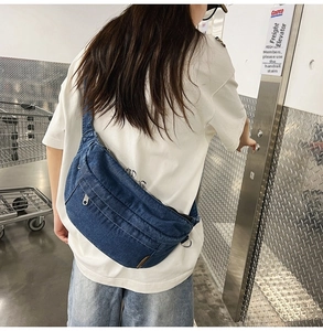 Street style shot of large blue denim crossbody bag with silver zippers and metal hardware
