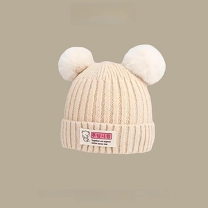 Close-up of beige knitted baby hat with double fur pom-poms and cute bear patch