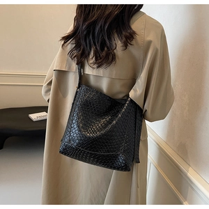 Close-up of black woven texture shoulder bag worn by model in a minimalist setting
