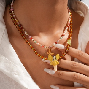 Detail of layered beaded necklace with fairy pendant, butterfly charm, and crystal beads