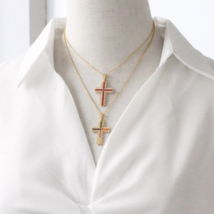 Close-up of layered gold necklaces with colorful zircon cross pendants on a white shirt