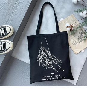 Detailed view of black canvas tote bag with white line art cat print on wooden floor