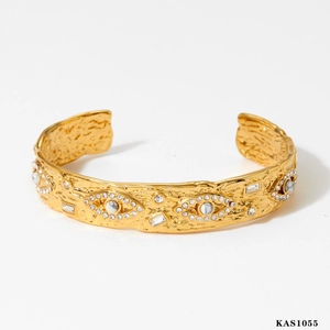 Bracciale rigido dorato testurizzato con motivi a occhio, pietre bianche e cristalli