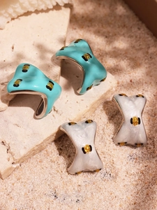 Macro view of C-shaped stainless steel earrings with turquoise and white enamel polka dots