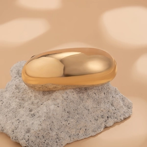 Close-up of a polished gold oval hair accessory on a minimalist stone display