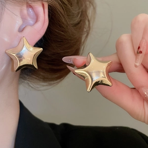 Macro shot of large metallic gold star-shaped stud earrings with mirror finish
