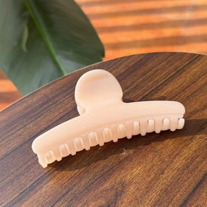 Elegant beige hair claw clip with linear texture on a wooden desk with leaf shadows