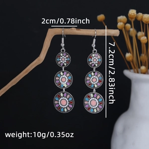 Detail of bohemian drop earrings with colorful enamel discs hanging on a branch
