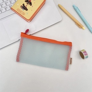 Close-up of a high-capacity orange mesh pencil case on a cozy desk with stationery