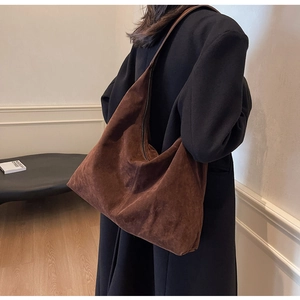 Detail of large brown suede tote bag with top zipper on black coat for winter commute