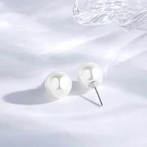 Detail of round white pearl earrings with silver posts on a flowing light background