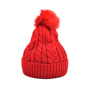 Gros plan détaillé sur la maille torsadée et le pompon en fourrure de ce bonnet rouge