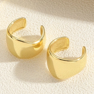 Macro detail of polished gold wide C-shaped ear cuff with smooth metallic finish