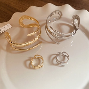 Macro detail of gold and silver spiral wave bracelets and rings on a white tray
