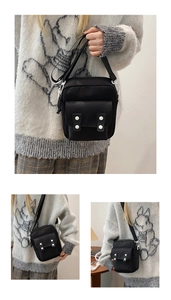 Detail view of the black canvas crossbody bag featuring white buckles and adjustable strap