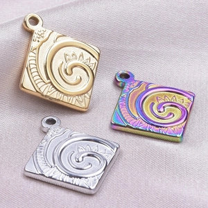 Macro shot of square stainless steel pendants with floral engraving in gold, silver, and rainbow