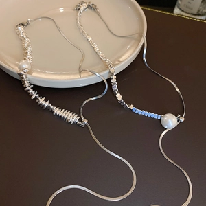 Detailed view of silver-toned pearl tassel necklaces on a textured ceramic plate