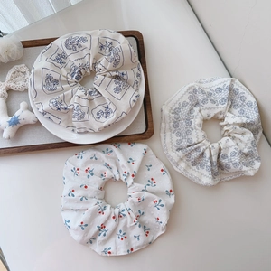 Three assorted cotton scrunchies with floral and berry prints on a wooden tray