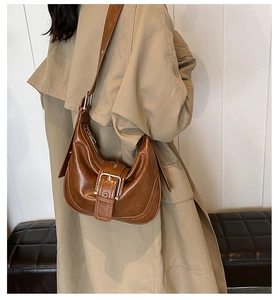 Brown vintage half-moon shoulder bag with metal buckle detail worn by a model