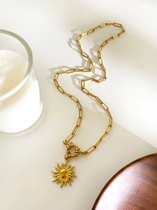 Close-up of golden sun pendant with paperclip chain and toggle clasp on a white background