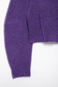 Dettaglio ravvicinato del maglione viola in maglia con cuciture bianche decorative