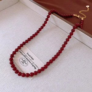 Detail of red beaded necklace with golden lobster clasp and heart charm on beige tray