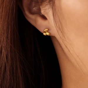 Macro shot of polished gold cherry stud earrings with 3D texture on a model's ear