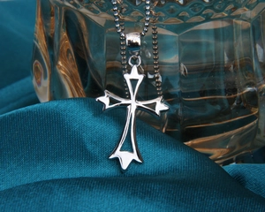 Détail macro du pendentif croix évidée en argent avec chaîne à billes sur soie bleue