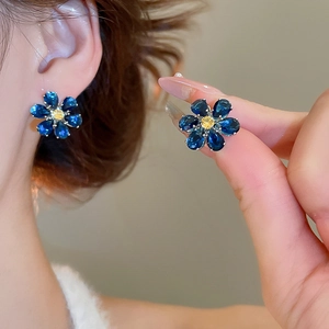 Detail of blue flower stud earrings with yellow center stone worn by a model