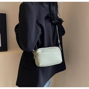 Side view of light green PU leather crossbody bag worn by a model in minimalist setting