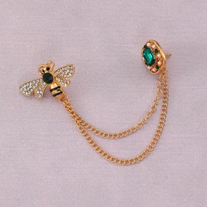 Close-up of vintage bee brooch with green emerald gems and double golden chains
