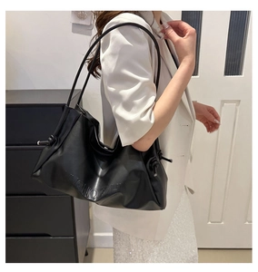 Detail of black pleated faux leather tote bag showing side drawstring and brand lettering