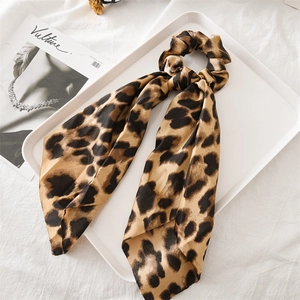 Close-up of a leopard print satin hair scrunchie with ribbon on a white tray and magazine