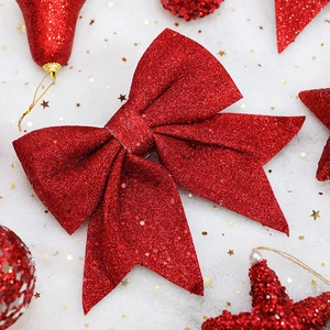 Sparkling red glitter Christmas bow with festive bells and stars on snowy background