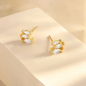 Detailed macro view of gold-plated stud earrings featuring marquise-cut zircons on a stone pedestal