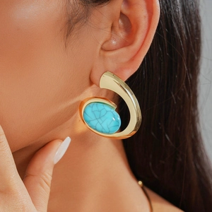 Close-up of bohemian gold drop earrings with textured blue stone inlay on a model
