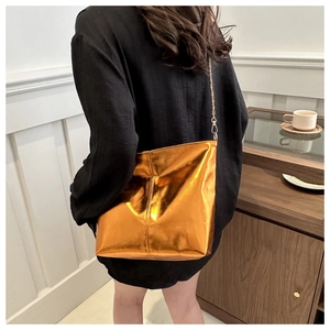 Detailed view of metallic gold tote bag with chain strap worn by model in minimalist setting