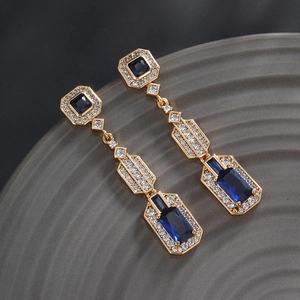 Macro shot of long gold geometric drop earrings with deep blue gemstones and white zircons