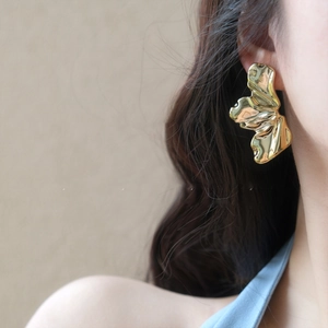 Detailed view of irregular gold leaf earrings with textured pleats on a model