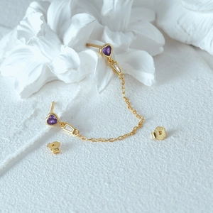 Macro shot of 925 silver gold-plated heart earrings with purple zircon on white backdrop